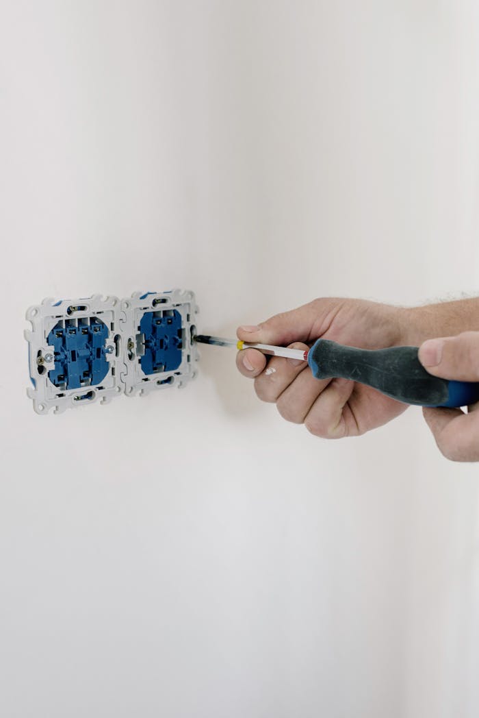 services-03 Close-up of hands using a screwdriver to install electrical sockets on a white wall.